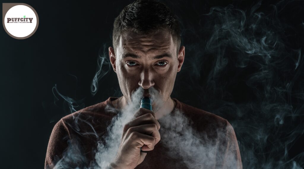 A man inhales a vape through his mouth and exhales a lot of smoke through his nose.