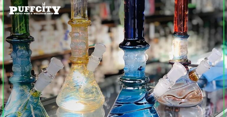 This image is showing Four colored glass water pipes are placed on a shelf in the smoke shop. One in orange, one in red, and two in blue.