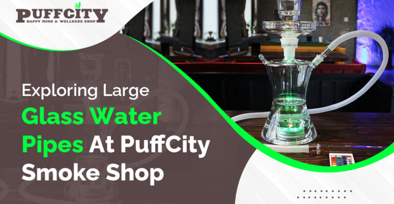 In this photo, a large glass water pipe is placed on a table. The background is gray and brown with the PuffCity logo.