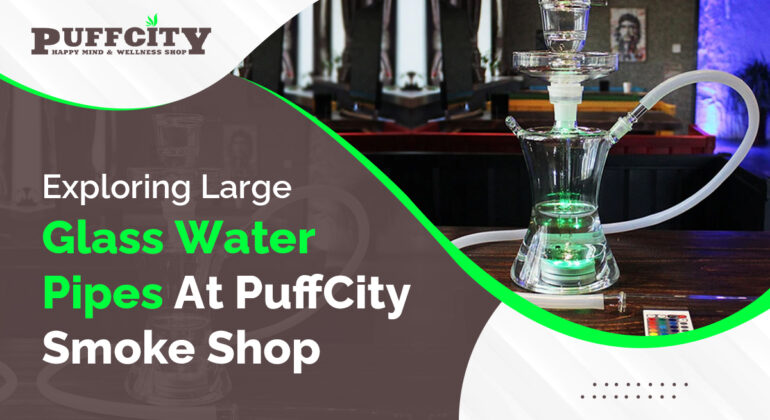 In this photo, a large glass water pipe is placed on a table. The background is gray and brown with the PuffCity logo.